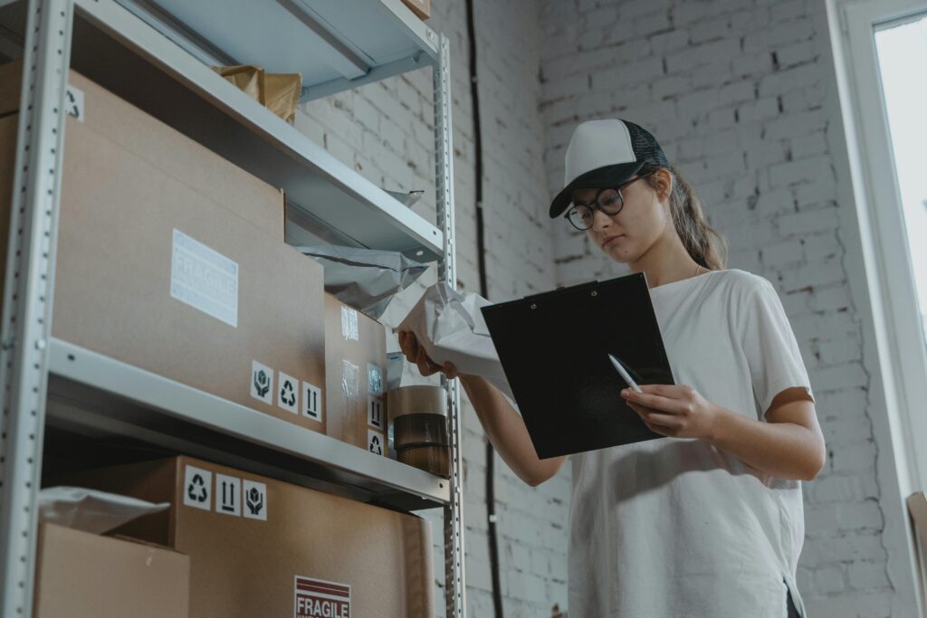 pexels-photo-6169027-6169027 Warehouse worker organizing packages on shelf with clipboard.